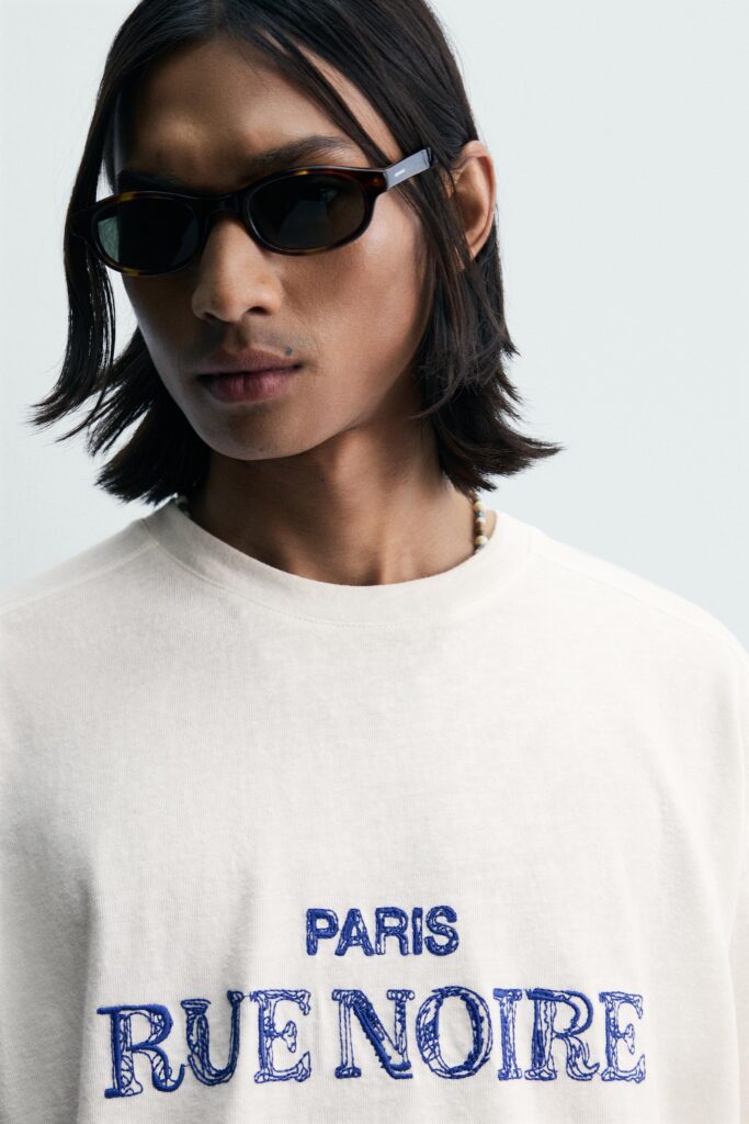 White t-shirt featuring blue embroidered typography artwork on front placement