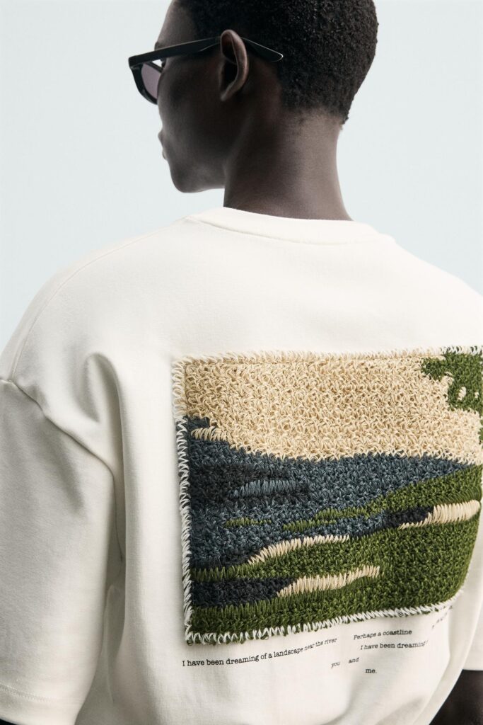White sweatshirt with textured crochet landscape artwork on the back.